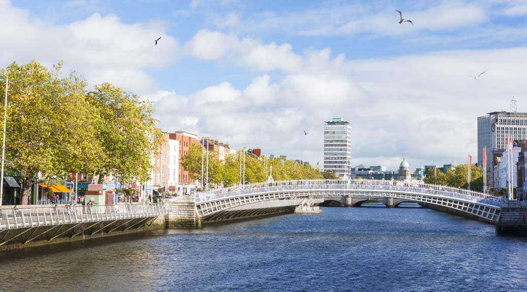 View of Hapenny Bridge in Dublin with green tress and buildings.